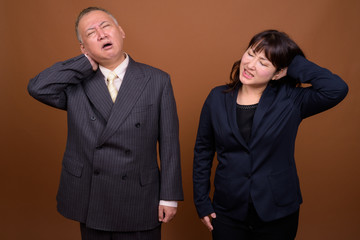 Stressed mature Asian businessman and mature Asian businesswoman getting neck pain together