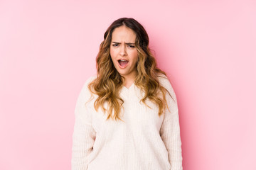 Young curvy woman posing in a pink background isolated screaming very angry and aggressive.