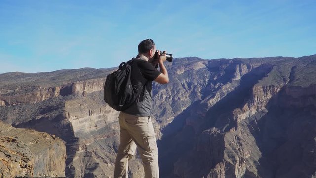 Young Foreign Male Tourist Taking Photos on Professional Camera of Wadi Ghul aka Grand Canyon of Oman in Jebel Shams Mountains. Man in Active Solo Travel in Middle East Countries