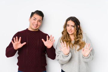 Young couple posing in a white background rejecting someone showing a gesture of disgust.