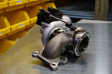 Modern turbocharger on a steel background. Turbocharger element allows you to significantly increase engine power using exhaust gases. Original high-quality spare parts for car repair.