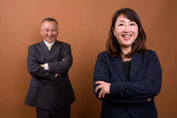 Happy mature Asian businessman and mature Asian businesswoman with arms crossed together
