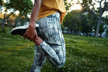 Fototapeta premium Close-up of woman in sportswear stretching her leg in the park - woman stretching her quads before a run
