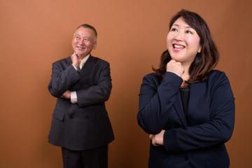 Happy mature Asian businessman and mature Asian businesswoman thinking together