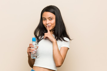 Young asian woman holding a water bottle keeping a secret or asking for silence.