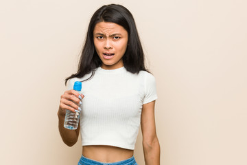 Young asian woman holding a water bottle screaming very angry and aggressive.