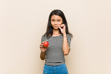 Young asian woman holding an apple with fingers on lips keeping a secret.