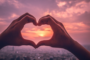Plakat A hands in the form of heart love. Sign of valentine day at sunset with landscape view of city