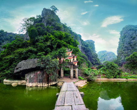 Outdoor park landscape with lake and stone bridge. Gate entrance to ancient Bich Dong pagoda complex dating to 1428. Ninh Binh, Vietnam travel destination - Powered by Adobe