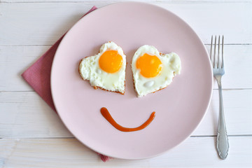 Two fried eggs on pink plate for healthy breakfast on wooden table. top view