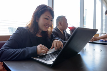 Mature Asian businessman and mature Asian businesswoman using laptop at restaurant together