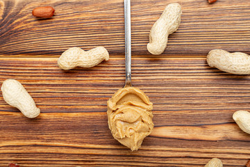 Vintage spoon with creamy peanut butter on a brown wooden table. Near the peanut butter lies peanuts in the shell and peeled peanuts. Flat lay of peanut paste for cooking breakfast.Vegan food concept