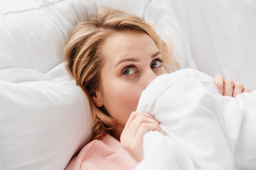 Woman indoors at home hiding face under blanket.