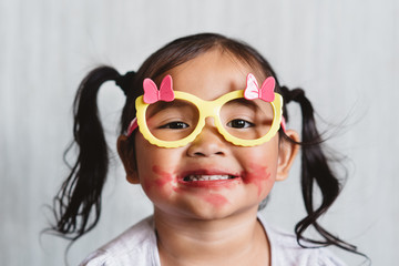 Cute little asian girl playing with lipstick makeup and applying lipstick to her lips. Concept of beauty and childhood