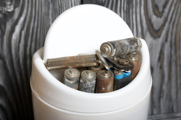 Waste bin. It contains finger-type batteries coated with corrosion. Against the background of brushed pine boards painted in black and white.
