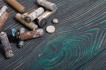 Spent finger-type batteries coated with corrosion. They lie on brushed pine boards painted in black and green.