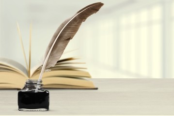 Feather quill pen and glass inkwell with the open book