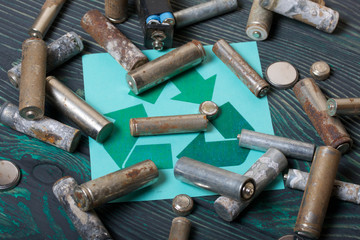 Spent finger-type batteries coated with corrosion. Waste recycling sign. They lie on brushed pine...