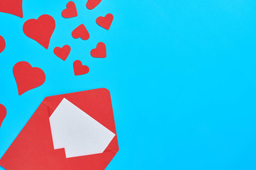 Red hearts near open postal envelope with blank white paper on blue desk. Love message. Concept of Valentines Day. Space for text. Top view