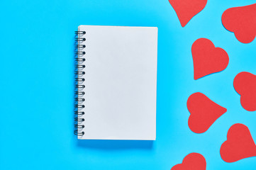Blank notebook and red paper hearts on blue desk. Love message. Concept of Valentines Day. Space for text. Top view