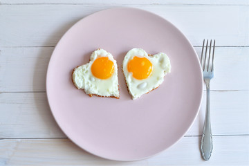 Two fried eggs on pink plate for healthy breakfast on wooden table. top view