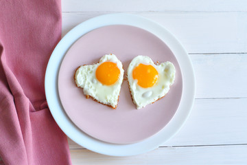 Two fried eggs on pink plate for healthy breakfast on wooden table. top view