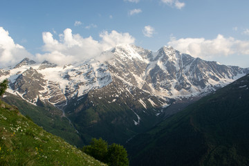 huge snowy mountain covered with thick white clouds and glaciers from which mountain waterfalls...