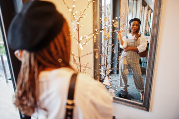 African american woman in overalls and beret against mirror in soft light room.