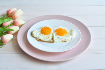 Breakfast on Valentine's Day - fried eggs in the shape of a heart and bouquet of pink tulips.top view
