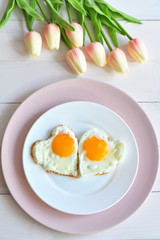 Breakfast on Valentine's Day - fried eggs in the shape of a heart and bouquet of pink tulips.top view