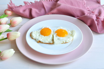 Breakfast on Valentine's Day - fried eggs in the shape of a heart and bouquet of pink tulips.top view