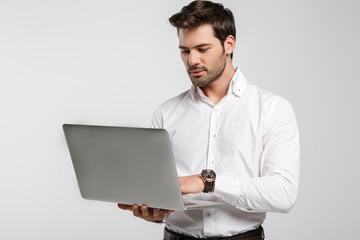 Image of young successful businessman holding and using laptop