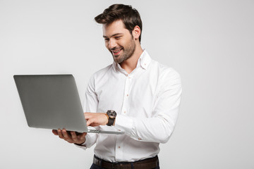 Image of young cheerful businessman holding and using laptop