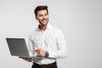 Image of young cheerful businessman holding and using laptop