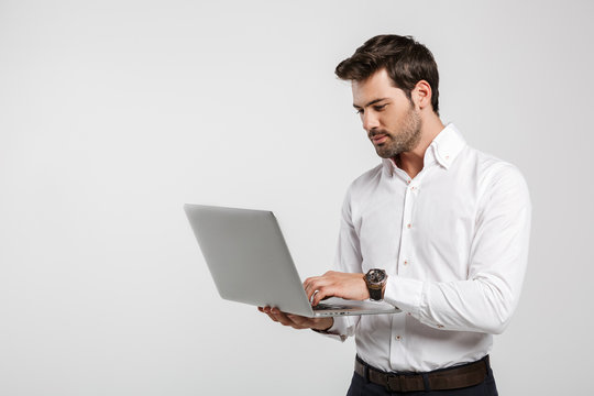 Image of young successful businessman holding and using laptop