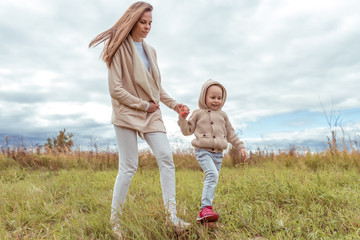 Fototapeta premium Woman mother walks with the child, little son boy 4-5 years old, autumn day outdoors in the park, background field grass and lawn, casual warm clothes with a hood.