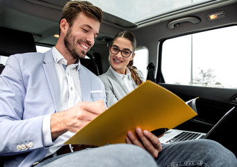 Young business people working together while traveling by a car. They are using laptop and preparing for meeting.	