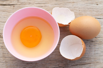 Broken egg shells and eggs on bowl, raw egg in small bowl at wooden background menu and recipe.