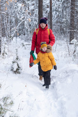Dad and son in bright jackets make their way through the snow in the winter white forest