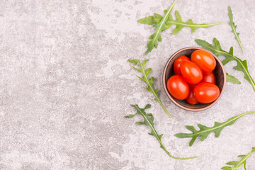 Red cherry tomatoes and fresh arugula leaves on a grey textured stone background, empty copy space