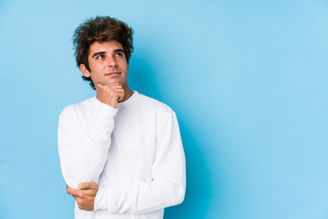 Young caucasian man against a blue background isolated looking sideways with doubtful and skeptical...