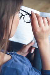 A woman with vision problems is reading a book with glasses.
