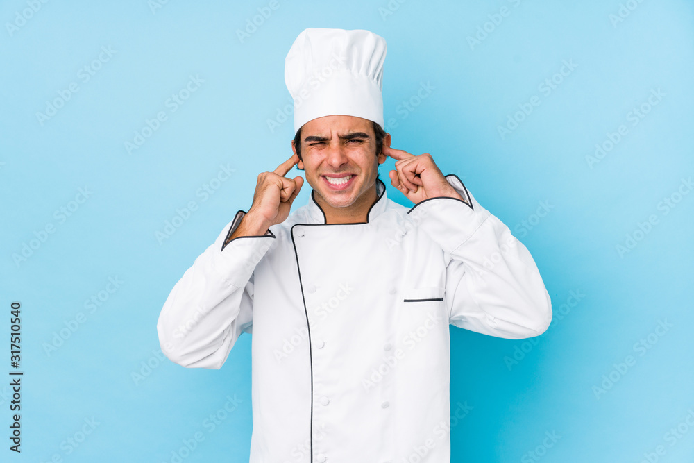 Wall mural young cook man isolated covering ears with hands.