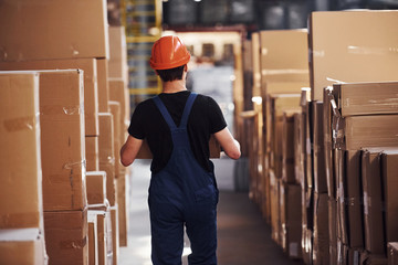 Young storage worker in uniform and hard hat carries box in hands