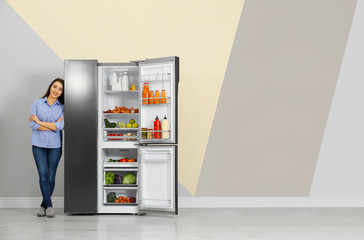 Happy young woman near open refrigerator indoors, space for text