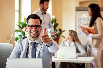 Portrait of businessman at the office looking at camera and showing thumbs up.