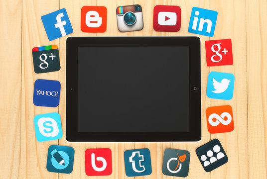 KIEV, UKRAINE - JULY 01, 2015: Famous social media icons such as: Facebook, Twitter, Blogger, Linkedin, Google Plus, Myspace and others. printed on paper and placed around iPad on wooden background.
