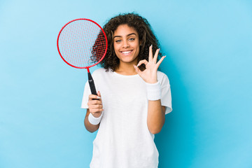 Young african american woman playing badminton cheerful and confident showing ok gesture.