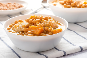 Curry with chickpeas, pumpkin, zucchini and cauliflower in white bowls on the table. Vegetarian curry with stewed vegetables. Traditional indian cuisine, vegan food.