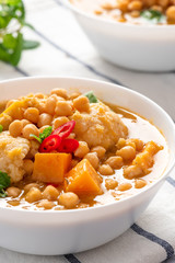 Curry with chickpeas, pumpkin, zucchini and cauliflower in white bowls on the table. Vegetarian curry with stewed vegetables. Traditional indian cuisine, vegan food.